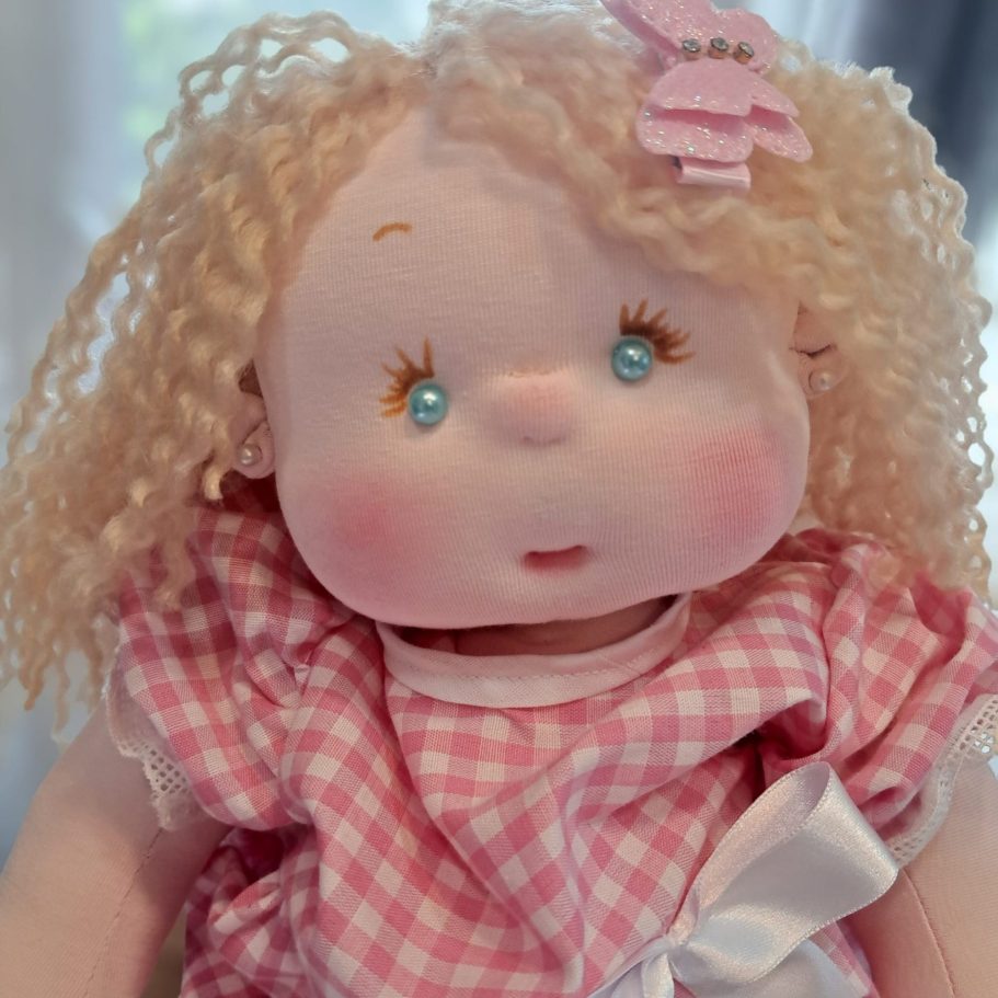 Muñeca de trapo con cabello rizado, vestido a cuadros y un clip en el cabello.