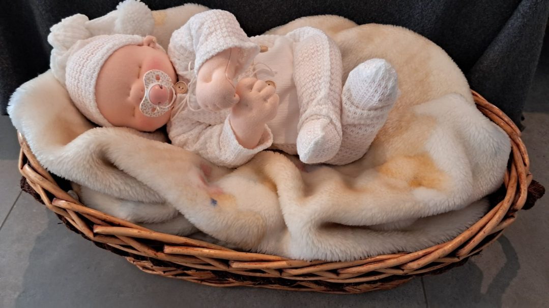 Bebé de tela con conjunto de punto blanco y chupete, dormido en una cesta de mimbre